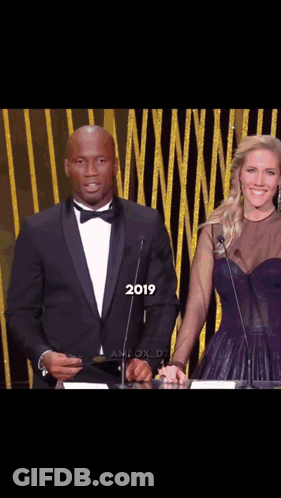 Man In Tuxedo And Woman In Purple Dress At Podium 2019 GIF
