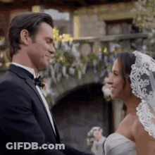 Man In Tuxedo And Woman In Wedding Dress Smiling At Each Other GIF