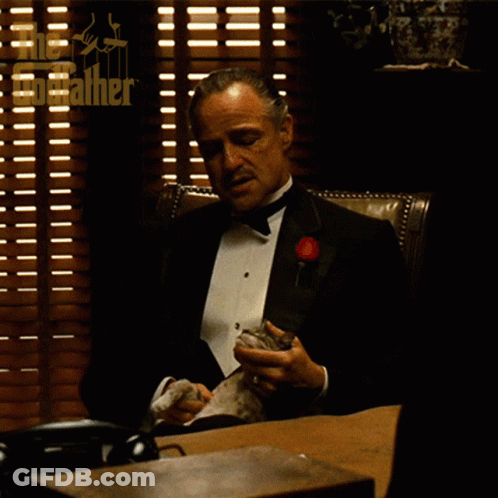 Man In Tuxedo At Desk With Blinds And Godfather Logo GIF
