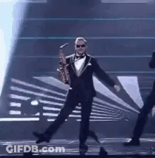 Man In Tuxedo Holding Saxophone On Stage GIF