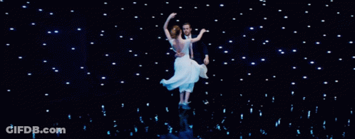 Man In Tuxedo Holding Woman In White Dress On Stage GIF