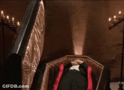 Man In Tuxedo Lying In Coffin With Red Cape GIF