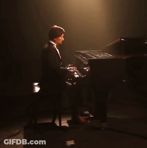 Man In Tuxedo Playing Piano In Dark GIF