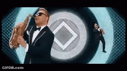 Man In Tuxedo Playing Saxophone With Another Man Behind GIF