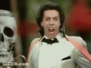 Man In Tuxedo Screaming With Bat On Neck In Front Of Skeleton GIF