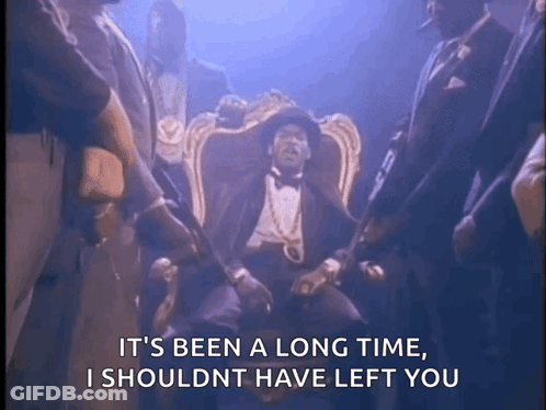 Man In Tuxedo Sitting With Standing Men GIF