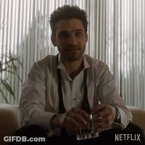 Man In Tuxedo Sitting With Whiskey In Front Of Netflix Sign GIF