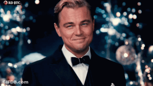 Man In Tuxedo Smiling In Front Of RD BTC Banner GIF