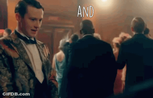 Man In Tuxedo Standing Before Crowd With Word And GIF