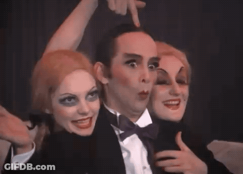 Man In Tuxedo Surrounded By Two Women With Makeup GIF