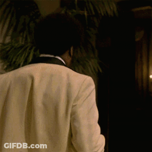 Man In Tuxedo Walking In Dark Room With Palm Tree GIF