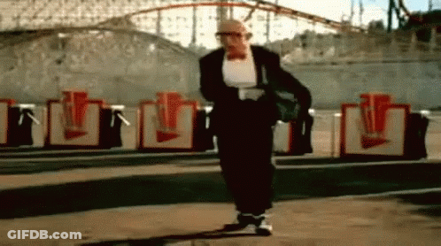 Man In Tuxedo Walking Past Roller Coaster GIF