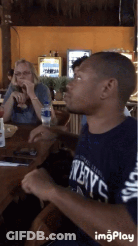Man In Twelve C Shirt Sitting At Table GIF