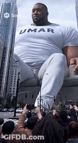 Man In Umar Shirt Sitting On Couch In Crowd GIF