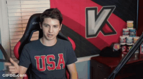 Man In USA Shirt Sitting In Front Of Large K GIF