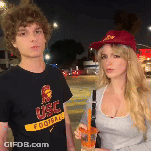 Man In USC Football Shirt Next To Woman In Red Hat GIF