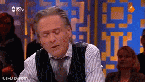 Man In Vest And Tie Sitting In Front Of KRO Screen GIF