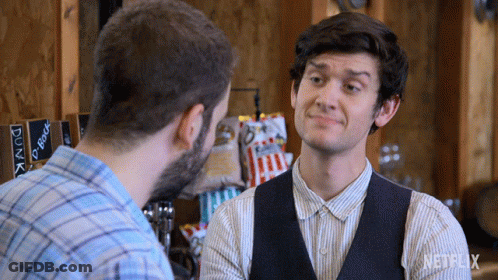 Man In Vest Talks To Another In Front Of Netflix Sign GIF