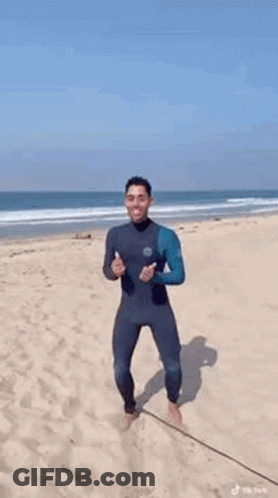 Man In Wetsuit Dancing On Beach GIF