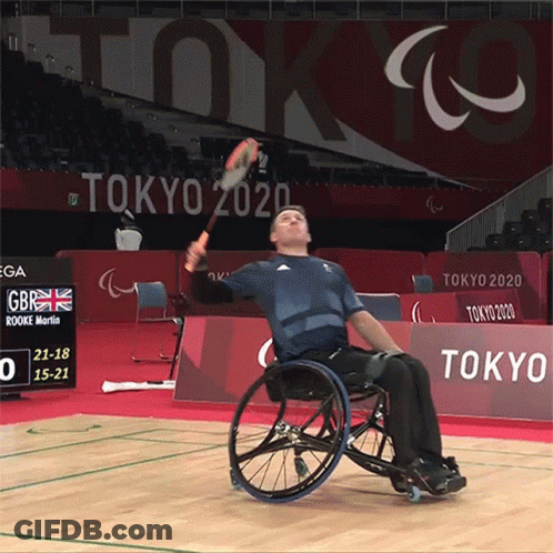 Man In Wheelchair Holding Tennis Racquet In Front Of Tokyo 2020 Sign GIF