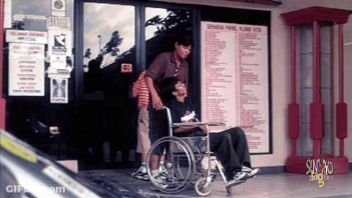 Man In Wheelchair Pushed By Man In Brown Shirt GIF
