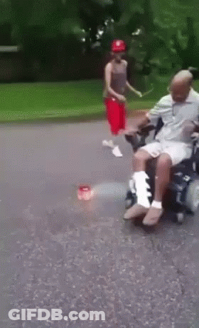 Man In Wheelchair Pushed By Woman In Red Hat GIF