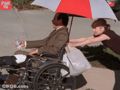 Man In Wheelchair Pushed By Woman Under Umbrella GIF