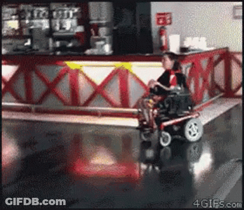 Man In Wheelchair Riding Past Red And White Counter GIF