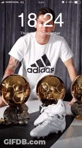 Man In White Adidas Shirt Surrounded By Soccer Balls And Cleats GIF