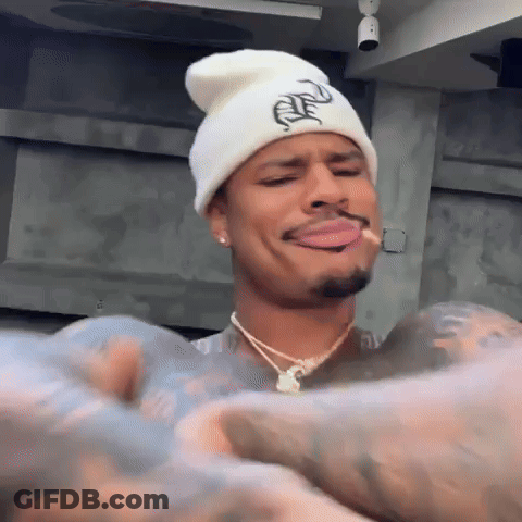 Man In White Beanie And Necklace Smoking Cigarette Making Funny Face GIF