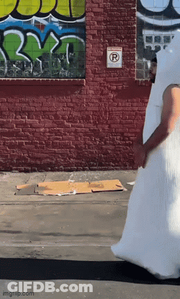 Man In White Costume Walking Past Graffiti Wall GIF