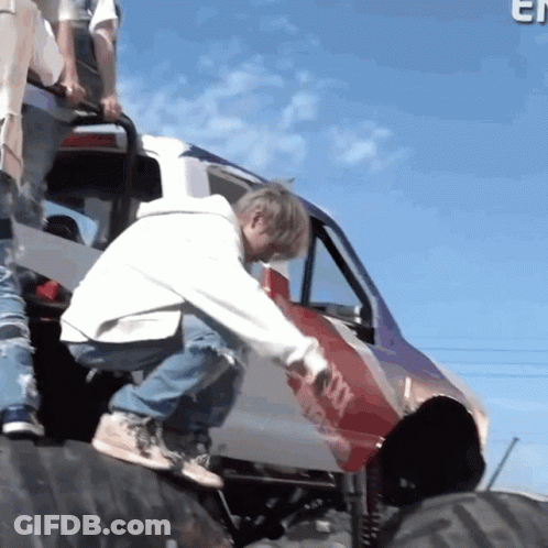 Man In White Hoodie Kneeling On Tire Next To Jeep GIF