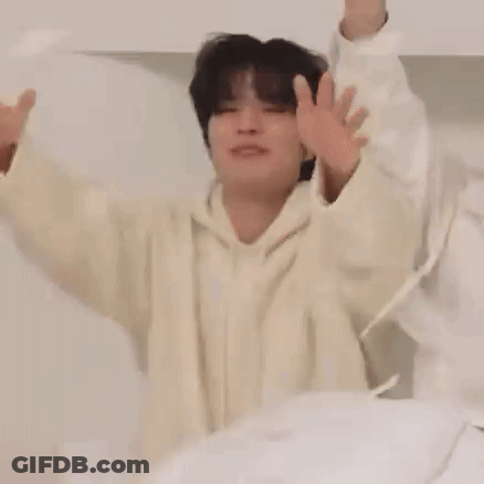 Man In White Hoodie Sitting On Bed With Arms Up GIF