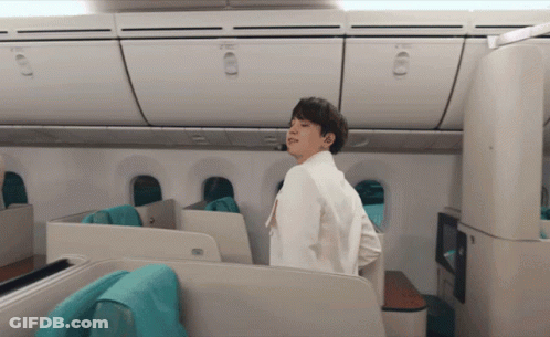 Man In White Jacket Standing In Airplane Looking At Camera GIF