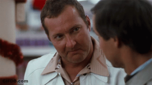 Man In White Jacket Talking To Man In Brown Shirt GIF