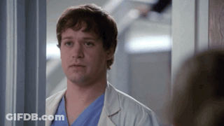 Man In White Lab Coat And Blue Scrubs In Hallway GIF
