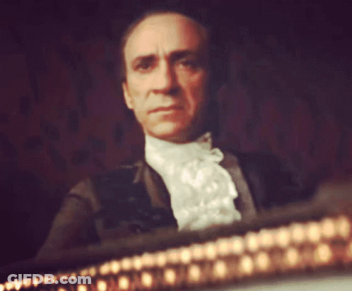 Man In White Lace Collared Shirt Sitting In Dark Room GIF