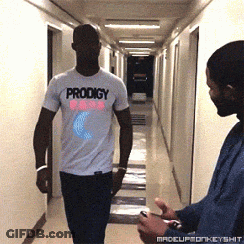 Man In White Prodigy T-Shirt Walking Down Hallway GIF