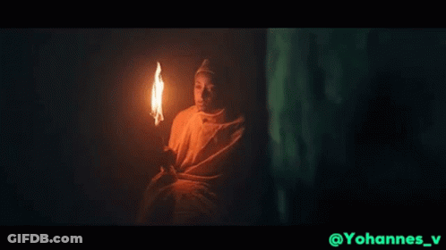 Man In White Robe Holding Torch In Dark GIF