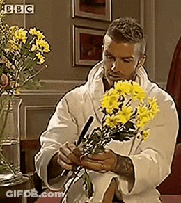 Man In White Robe Holding Yellow Flowers At BBC Sign GIF