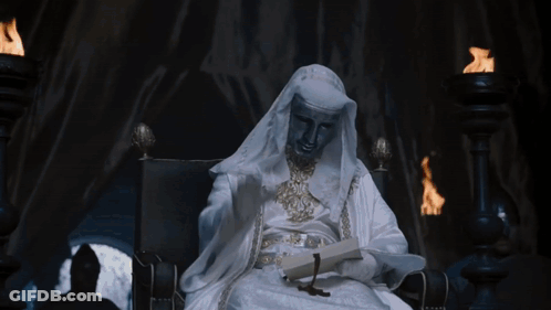 Man In White Robe Sitting In Chair Holding Book GIF