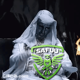 Man In White Robe Sitting In Front Of Fire With Safuu Logo GIF