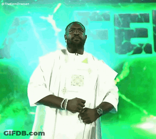 Man In White Robe Standing In Front Of Green Sign Saying EE GIF