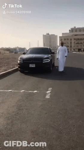 Man In White Robe Walking In Front Of Black Car With License Plate J RSMJ GIF