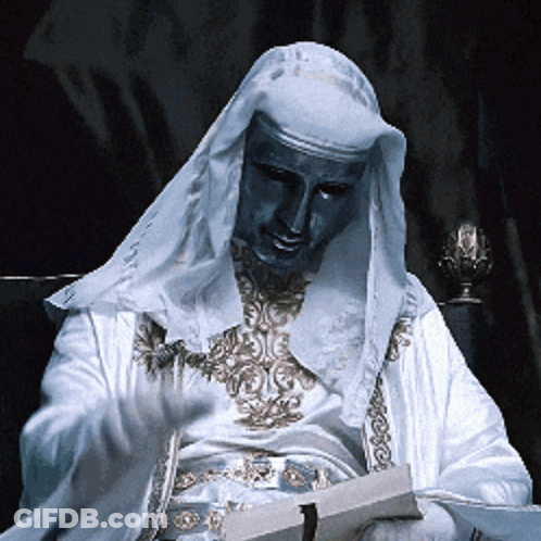 Man In White Robe With Blue Mask Reading Book GIF