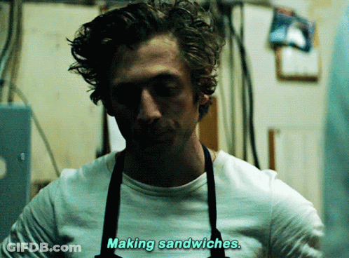 Man In White Shirt And Blue Apron Looking At Camera GIF