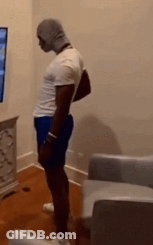 Man In White Shirt And Blue Shorts Standing In Front Of TV GIF