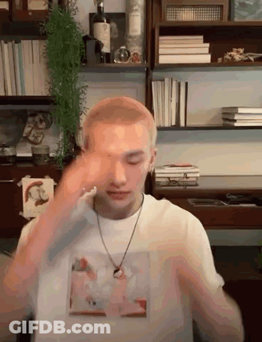 Man In White Shirt And Necklace By Bookshelf GIF