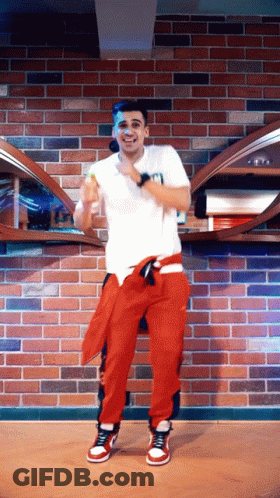 Man In White Shirt And Red Pants Dancing In Front Of Brick Wall GIF