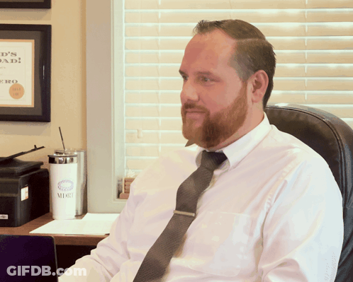 Man In White Shirt And Tie Sitting In Front Of Dad Sign GIF